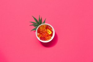 Cannabis gummy bears in white bowl with leaf on colorful orange background, copy space, background texture, legal cbd medical jelly concept
